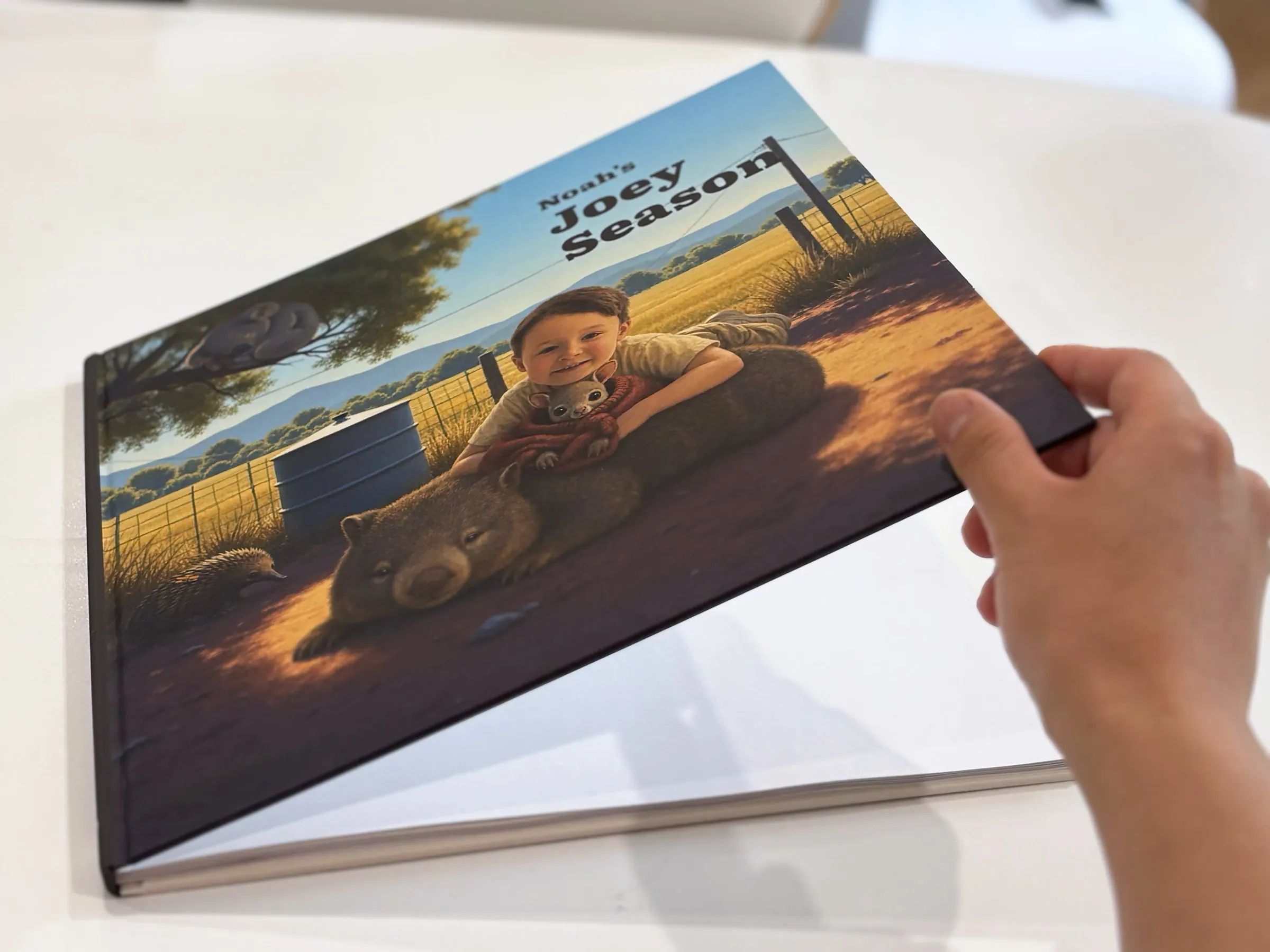 A hand lifting the cover of a printed Joey Season book.